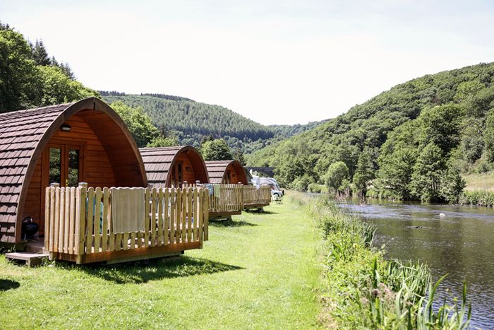 A photo of 3 small wooden cabins at the Camping Bissen located in the Heiderscheider Grund, surrounded by greenery and woods, and basking in the sunshine.